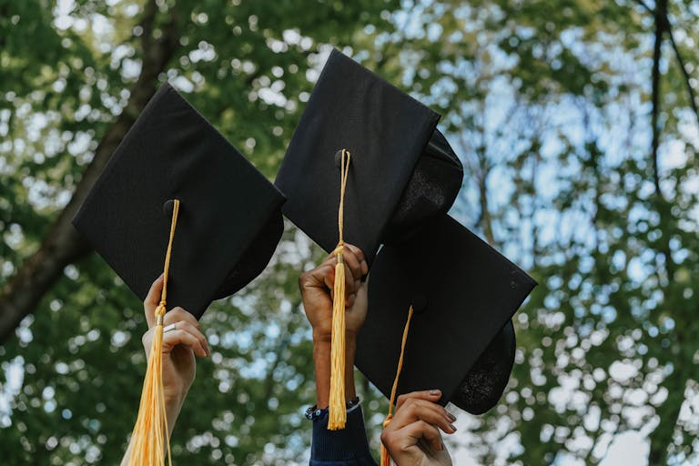 Three hands holding graduation caps in celebration for graduation weekend dining